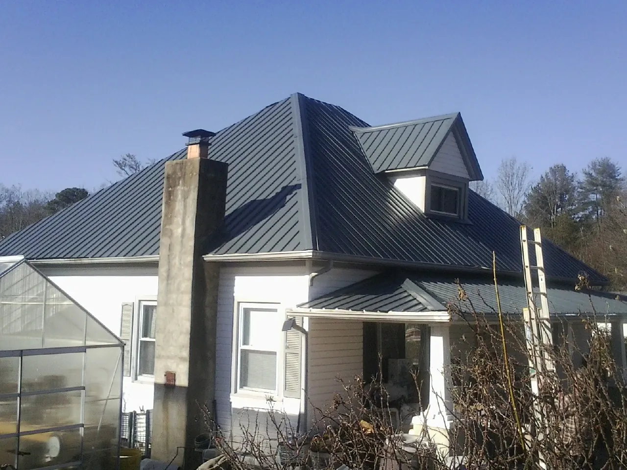 Dark blue standing seam metal roof on a white farmhouse with dormer — Slate & Tile Roof Repair by Roofing Brothers in North Providence