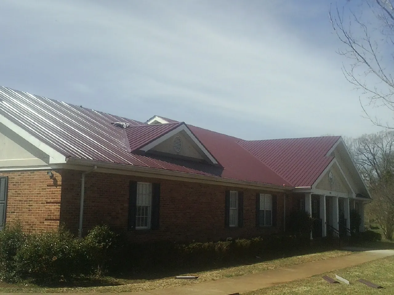 Red metal roof with gabled entries on a long brick building, from a Hail Damage Roof Repair job in North Providence