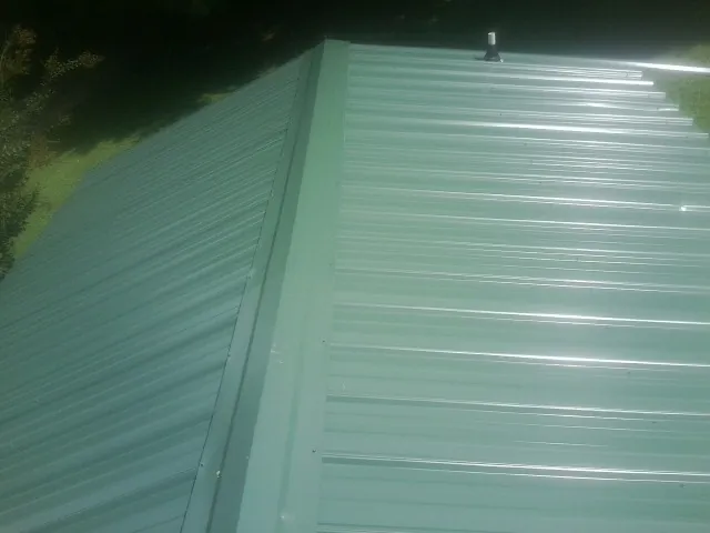 New green metal panels meeting at the ridge of a roof — Flat Roof Repair work by our crew in North Providence