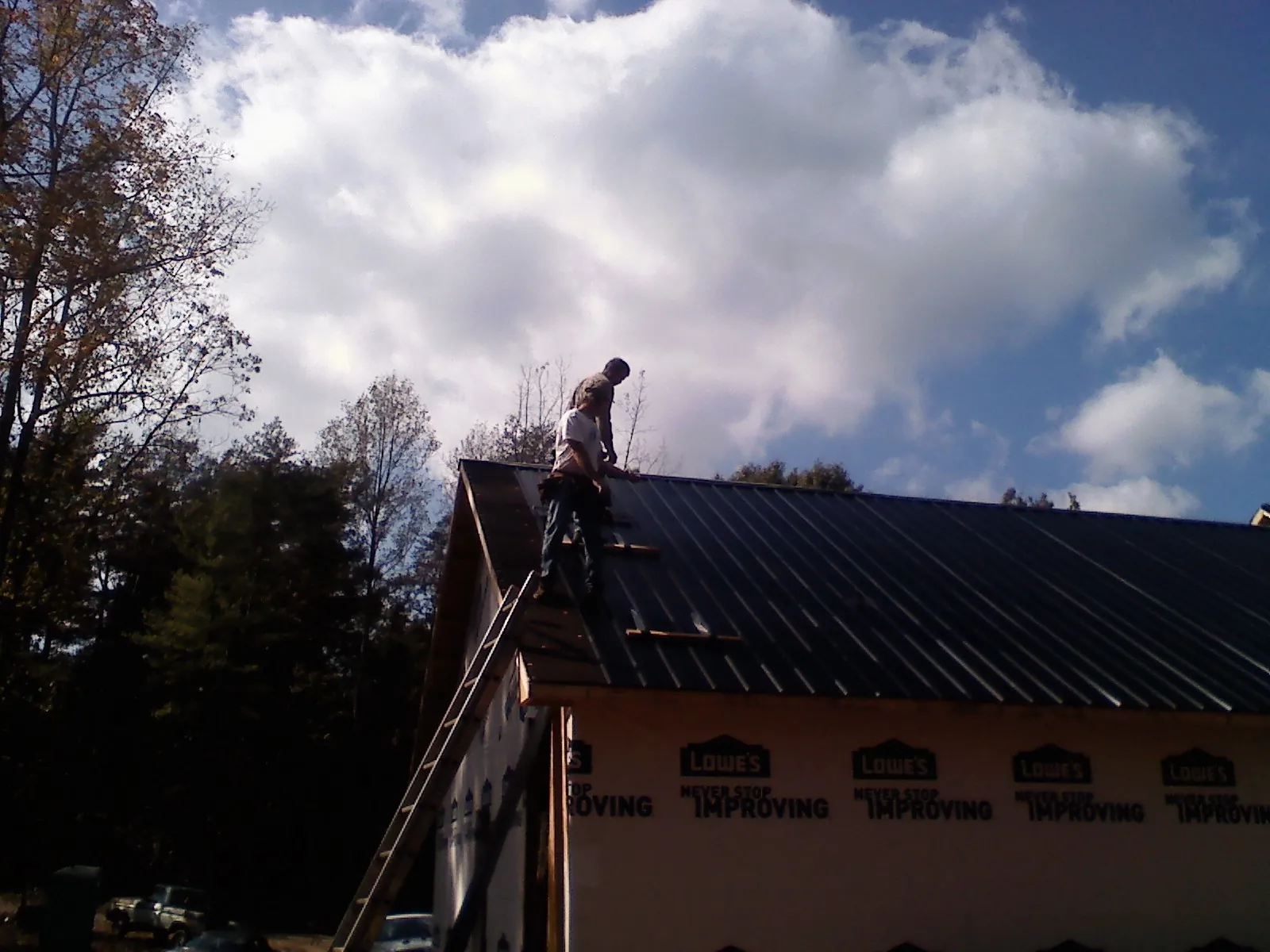 Roofer fastening dark metal panels high against a cloudy sky, from a Roof Inspection job in North Providence