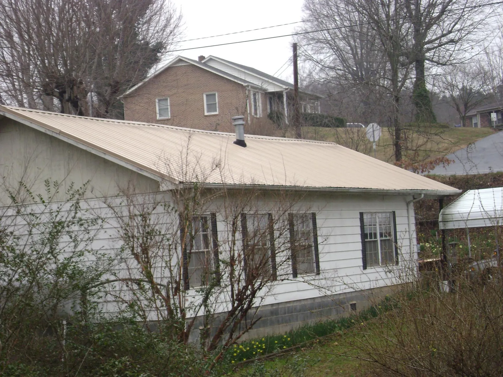 Tan metal roof on a white sided house set into a hillside — Commercial Roofing by Roofing Brothers in North Providence