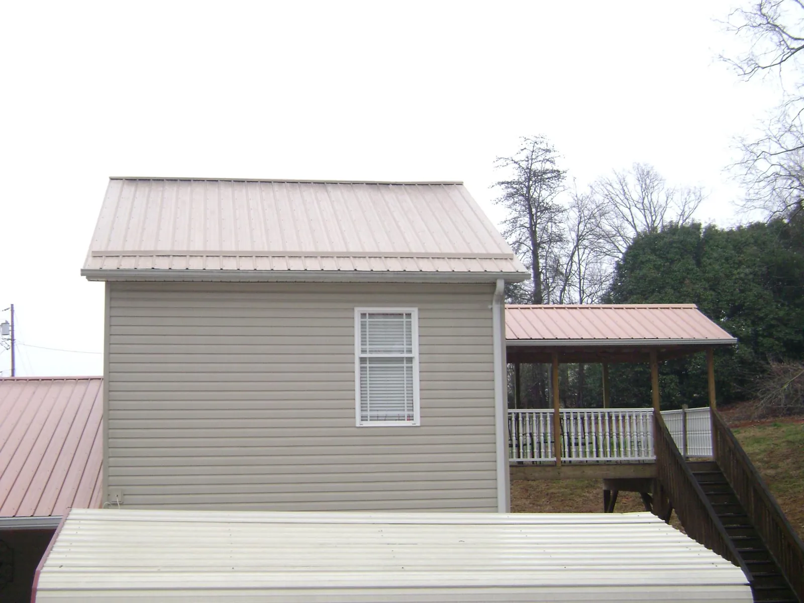 Tan metal roofs on a two story addition and attached porch, from a Roof Replacement job in North Providence